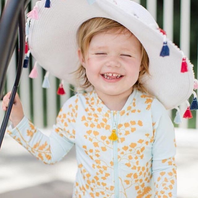 baby girl laughing in her Pink Chicken wan blue and fern printed swimsuit.