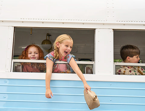 girl hanging out the window of a blue bus