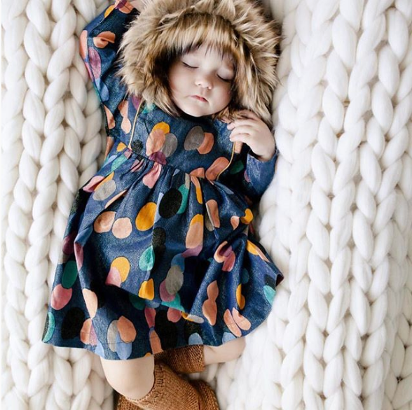 Sleeping baby wearing a fur hat and Pink Chicken polka dot dress
